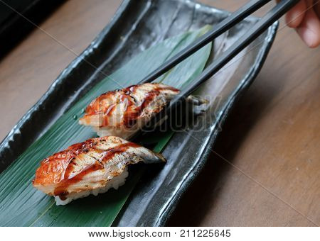 A hand picking up Unagi sushi from the plate.