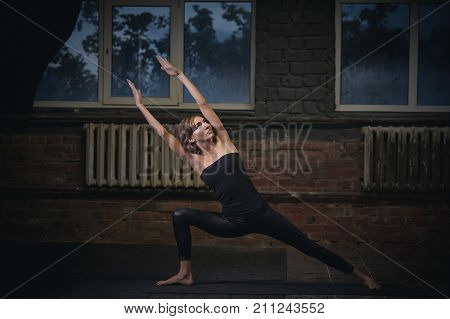 Beautiful sporty fit yogini woman practices yoga asana Utthita Parshvakonasana in the dark hall.