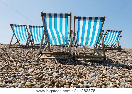 Classic striped blue and white deckchairs on the pebble beach and blue sky