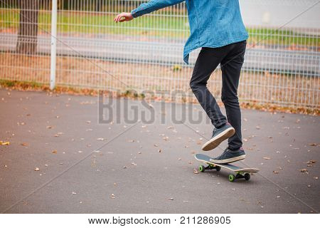 Young skate boy riding on the skate. Skateboarder doing trick in skating park on the nature background. Close-up of foot on the skate.