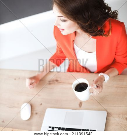 Attractive woman sitting at desk in office, working with laptop computer