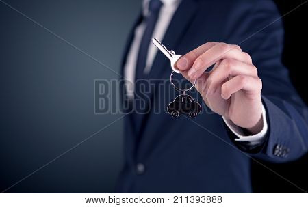 Young businessman hand over keys with empty dark background