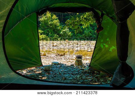 View of river in rocky ravine seen from tent of tourist camp in sunny summer day