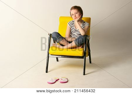 Dreaming young girl sitting on yellow chair. Shot of a little girl relaxing on a chair at home.
