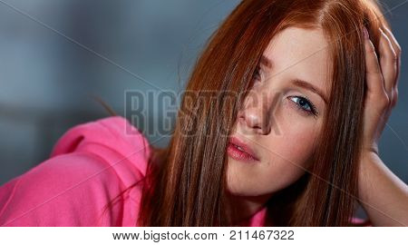 Portrait of wild ginger woman looking at camera, half face covered by hair.