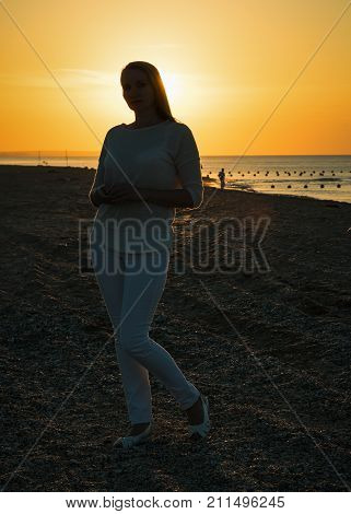 Beautiful woman in white clothes enjoying the sunset on the beach. Portrait of a beautiful woman by the sea.