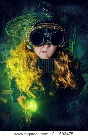 Happy Halloween. Cute child girl in witch costume is in a witch's lair. Cute funny witch girl wearing steampunk glasses.