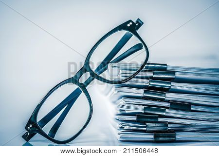 Close up black reading eyeglasses on stacking of office paper business working document and information data concept. retro color tone