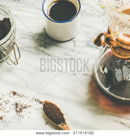 Morning black filtered coffee and white cup and coffee ground in jar on light grey marble table background, copy space, selective focus, square crop. Alternative coffee brewing concept