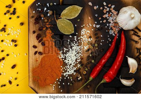 Composition with a cutting board, spices and hot pepper and garlic on a yellow background. Concept of food, spices, restaurant. Free space for text.