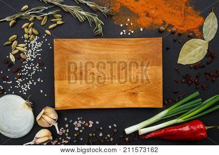 Composition with a cutting board, spices and hot pepper, onion and garlic on a black background. Concept of food, spices, restaurant.