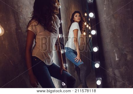 Sexy woman in a white t-shirt looks in the mirror. Mock-up.