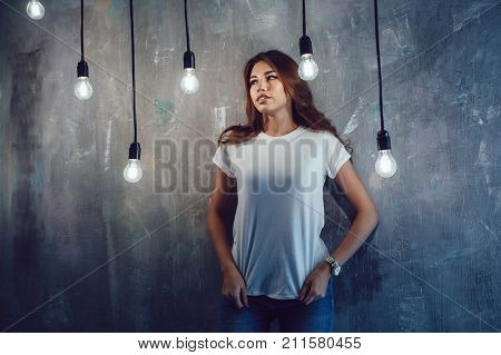 Sexy woman in a white T-shirt on a gray background with light bulbs. Mock-up.