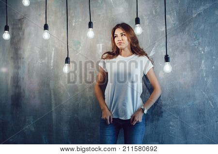 Sexy woman in a white T-shirt on a gray background with light bulbs. Mock-up.