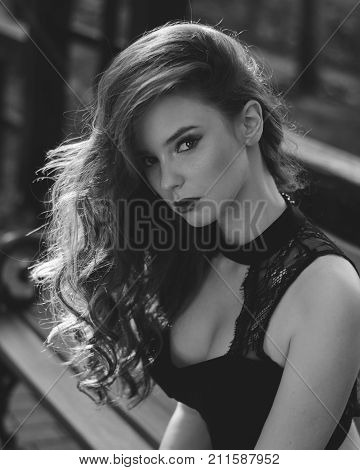 A black and white portrait of a sensual attractive young fashion model in a black dress, with long wavy healthy hair and a deep decollete. Fashion photo. Black and white photo.