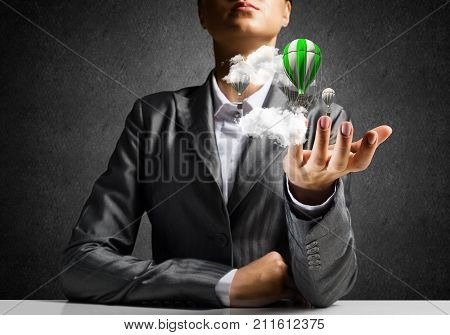 Closeup of business woman in suit presenting flying aerostate among clouds in her palm with dark wall on background. 
