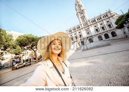 Young woman tourist in sunhat making selfie photo in front of the city hall building during the morning light in Porto, Portugal