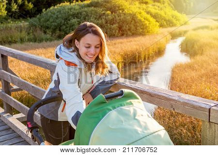 Young mother checking her baby in a stroller. Healthy perenting in the nature.