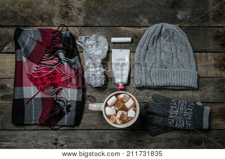 Selection of essentials for cold winter weather - hat. scarf, gloves, hot chocolate, rustic wood background. Winter survival kit