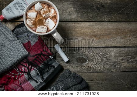 Selection of essentials for cold winter weather - hat. scarf, gloves, hot chocolate, rustic wood background. Winter survival kit