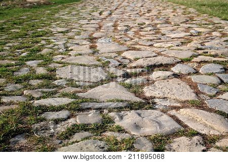 Ancient road paved with cobblestone and overgrown by grass. Closeup. Bottom view.