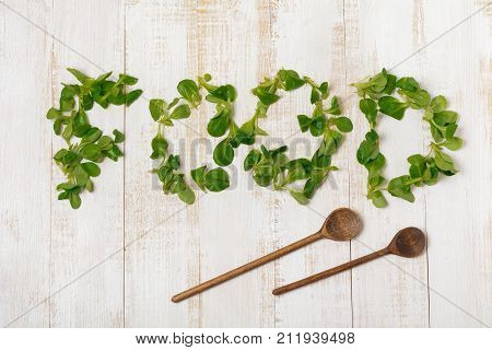 Word Food from Fresh raw salad leaves on light wooden background. Selective focus. Top view. Copy space.