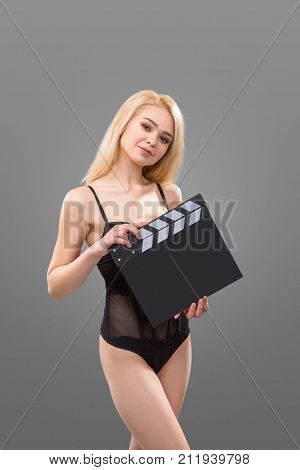 Close up a blond woman wearing in black lingerie holding a movie clapperboard over grey background