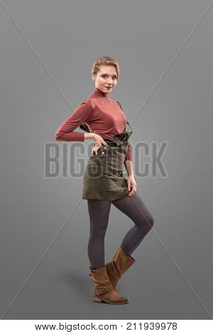 Fashion look of blonde girl dressed in casual style in short skirt and broun boots isolated on grey background