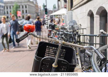 Focus on bicycle hanle bars and red bell in defocused blur background street scene with railing and unrecognizable people