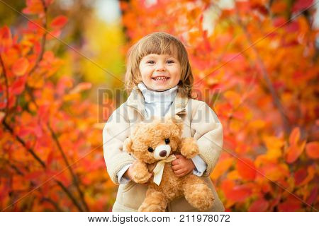 Little girl with a teddy bear in her hand on a background of autumn foliage. Autumn time
