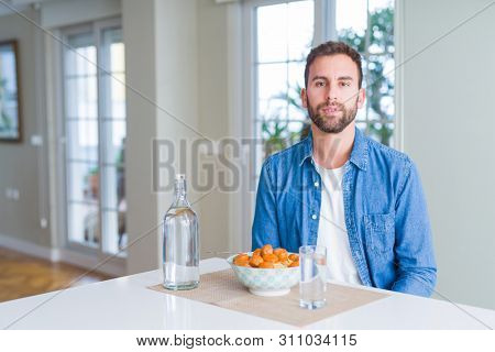 Handsome man eating pasta with meatballs and tomato sauce at home with serious expression on face. Simple and natural looking at the camera.