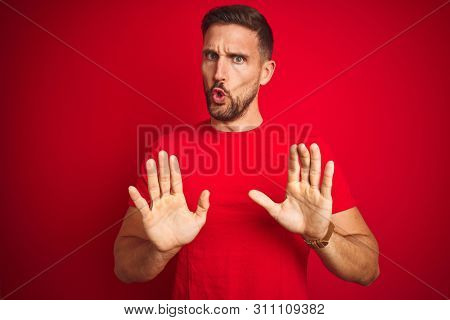 Young handsome man wearing casual t-shirt over red isolated background Moving away hands palms showing refusal and denial with afraid and disgusting expression. Stop and forbidden.