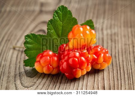 Few Berries Of Cloudberries With A Leaf On An Old Wooden Board Close-up