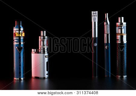 Electronic Cigarettes Or Vaping Devices On Black Background. Toned Light