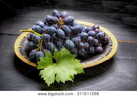 Bunch Of Ripe Blue-black Table Grapes With Leaf Served On Black Plate On Black Wooden Background