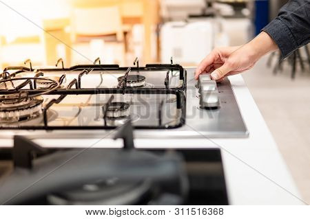 Male Hand Turning Switch Knob On Modern Gas Stove In Kitchen Showroom. Cooking Appliance In Domestic