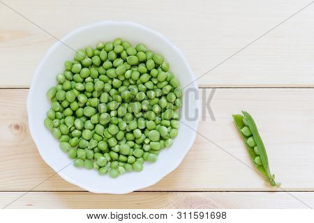 Green Peas Ready To Eat On White Plate On Light Wooden Table With Copy Space. Top View. Single Open 