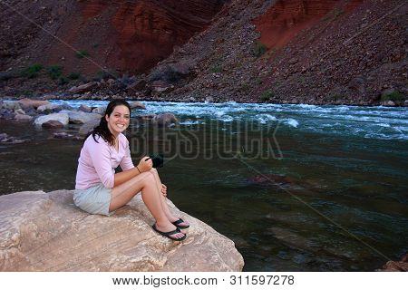 Young Woman Backpacker Resting On The Boulders By Hance Rapids In Grand Canyon National Park, Arizon
