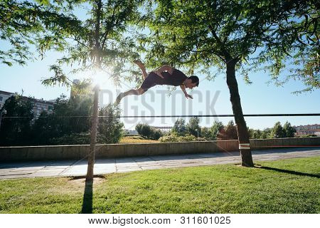 Man Training With Trickline Slackline In City Park