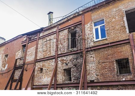 Brick Wall Of An Old House In Disrepair. To Avoid Collapse, The Wall Is Reinforced With A Metal Stru