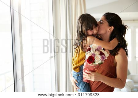 Mid adult woman holding her daughter, whoÃ¢â¬â¢s given her a bunch of flowers on her birthday, waist up