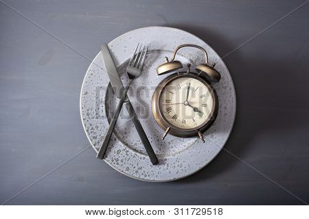 concept of intermittent fasting, ketogenic diet, weight loss. alarmclock fork and knife on a plate