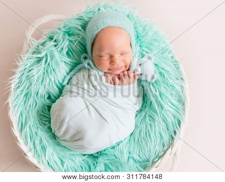 Lovely newborn resting in child sleeping basket with wool