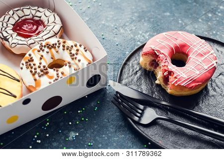 Pink Frosted Donut With Bite Missing On A Plate With Assortment Donuts Box On Dark Background. Top V