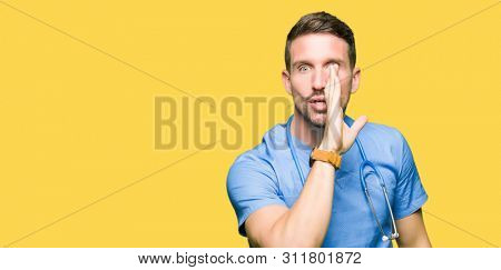 Handsome doctor man wearing medical uniform over isolated background hand on mouth telling secret rumor, whispering malicious talk conversation
