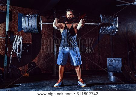 Muscular Bearded Tattoed Fitness Man Doing Deadlift A Barbell Over His Head In Modern Fitness Center
