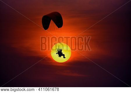 Silhouette Of The Paramotor Gliding And Flying In The Air Through Soft Sunlight Sunset Sky.