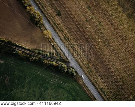Agricultural Landscape From Above, Which Is Crossed By Asphalt Road With One Moving Car. There Are S