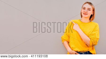 Horizontal Picture Of Young Good-looking Female Isolated On Grey Background, Pointing Leftwards With