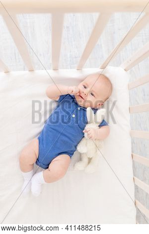 A Baby Boy In A Crib Lies On His Back, A Happy Newborn Wakes Up In The Morning Or Goes To Bed